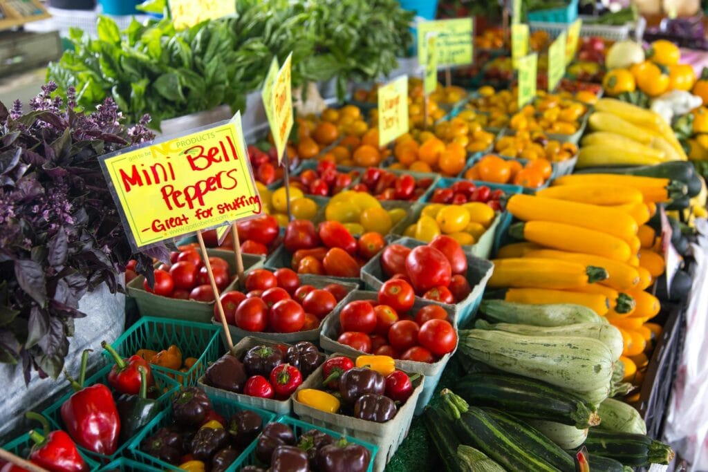A vibrant vegetable stand at a South African market displaying fresh produce including tomatoes, zucchinis, bell peppers, and squash.